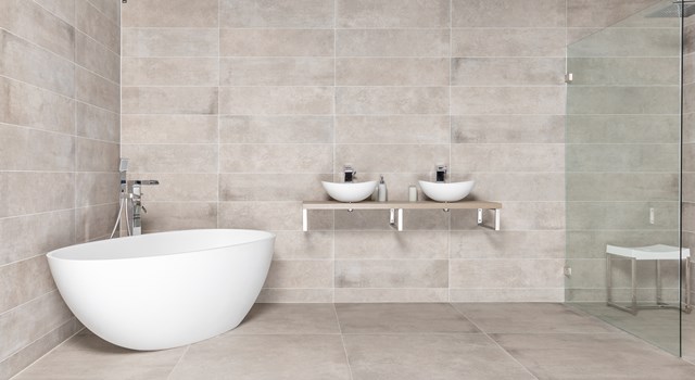 Free-standing white oval basin next to double basins, modern bathroom design with neutral beige tiles.