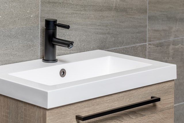 Wit keramisch wastafelblad met modern matzwart mengkraan, geplaatst op een houtlook badkamermeubel, ideaal voor een eigentijdse badkamer.