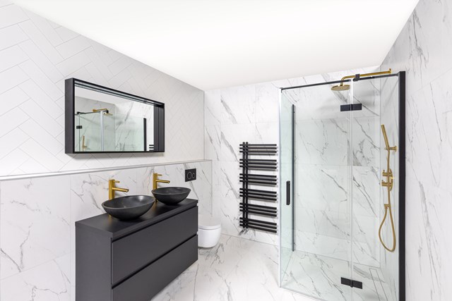 Moderne Badezimmer mit schwarzen Waschtischen, goldenen Armaturen, gläserner Duschwand und Marmorfliesen für eine luxuriöse Ausstrahlung.
