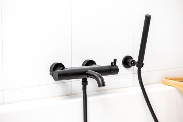 Matte black bath tap with handheld shower, modern design and round shapes, ideal as a stylish addition to the bathroom.