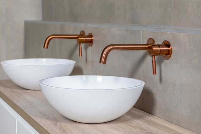 Weiße keramische Aufsatzwaschbecken mit runder Form, kombiniert mit stilvollen kupferfarbenen Wandarmaturen im modernen Badezimmer.