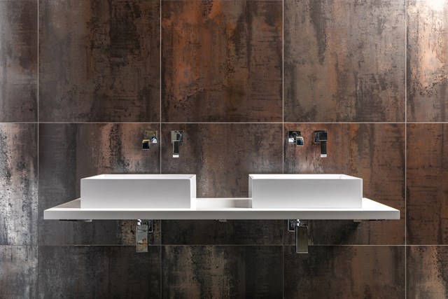 Witte dubbele wastafel op een strak wandmeubel tegen een bronskleurige betegelde muur in een moderne badkamer.