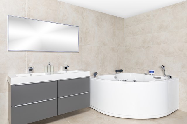 Moderne Badezimmer mit grauem Doppelwaschbecken, runder weißer Jacuzzi und großem Spiegel gegen helle Natursteine Wand.