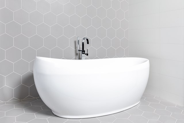 grijze-hexagon-tegels-vrijstaand-bad.jpg Vrijstaand ovaal wit ligbad met moderne chroomkraan, elegant design, perfect voor luxe badkamerinterieurs.