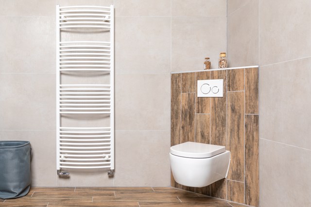 Witte handdoekradiator en hangend toilet met houtlook tegelafwerking in moderne badkamer.