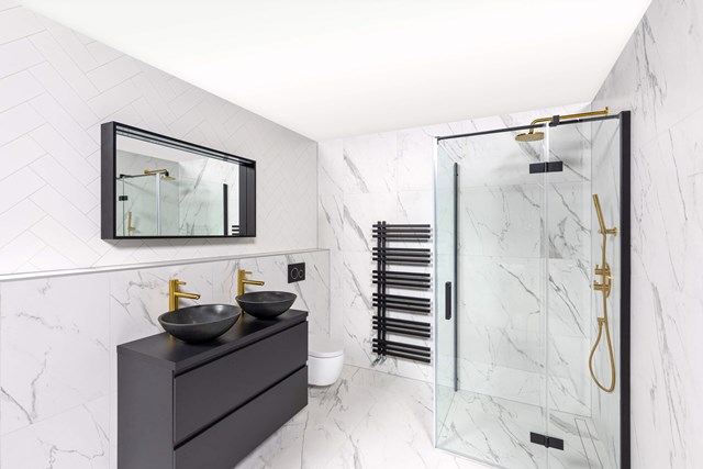 Moderne badkamer met marmeren wanden, glazen douchecabine, zwarte wastafelmeubels, dubbele waskommen en gouden kranen.
