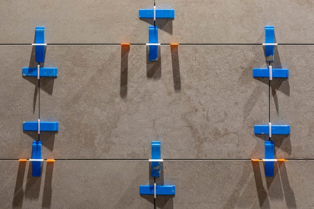 Blauwe tegelnivelleersysteem op grijze keramische tegels; precisie-tool voor perfecte tegelplaatsing in badkamerprojecten.