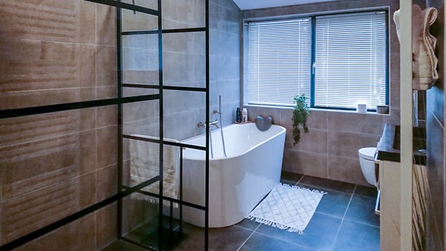 Moderne badkamer met vrijstaand wit bad, industriële zwarte glazen scheidingswand en houten wandpanelen.