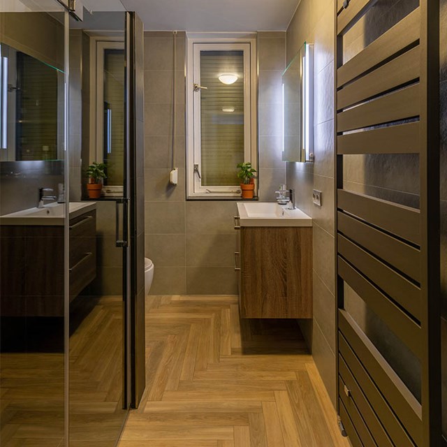 Modern bathroom with wooden vanity unit, design radiator and large mirror; stylishly decorated room with warm tones.