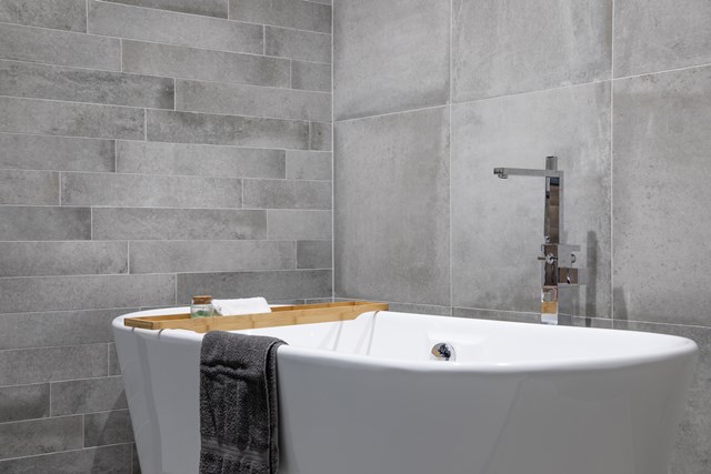 Vrijstaande witte ovalen badkuip met houten badplank, grijze tegels in moderne badkamer.