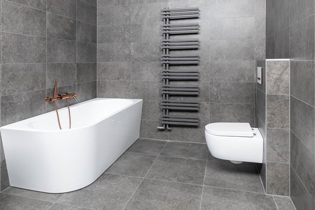 Strakke moderne Badezimmer mit freistehender weißer Badewanne, Wand-WC und schwarzem Handtuchheizkörper auf grauem Fliesenboden.