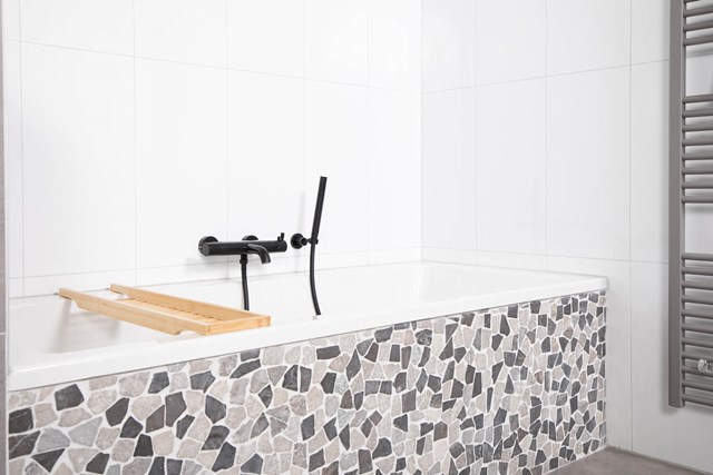 Weißes Bad mit Mosaikrand, ausgestattet mit schwarzer Badewannenarmatur und Holzplatte; modernes Design für luxuriöse Bäder.