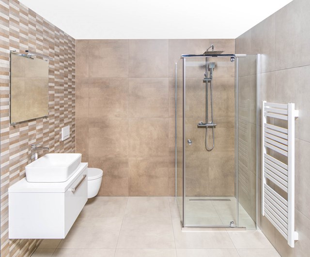 Moderne Badezimmer mit gläserner Duschwand, weißem Waschtisch, Design-Heizkörper und keramischen Wandfliesen in beigen Tönen.