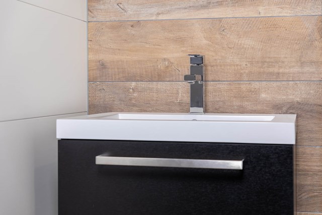 Schwarzes Badmöbel mit weißem Waschbecken und modernem chromfarbenem Wasserhahn, minimalistisches Design geeignet für kompakte Badezimmer.