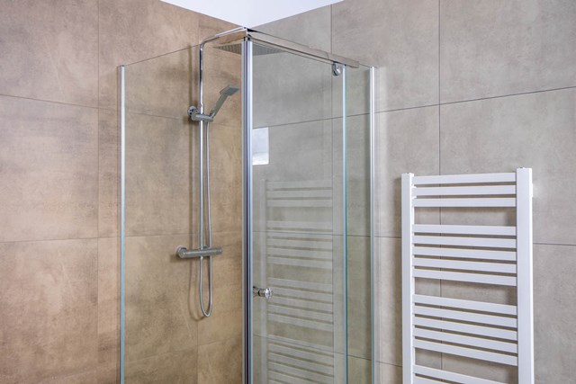 Glas Duschkabine mit chromatischen Details und moderner Regendusche, neben einem weißen Handtuchheizkörper in luxuriösem Badezimmer.