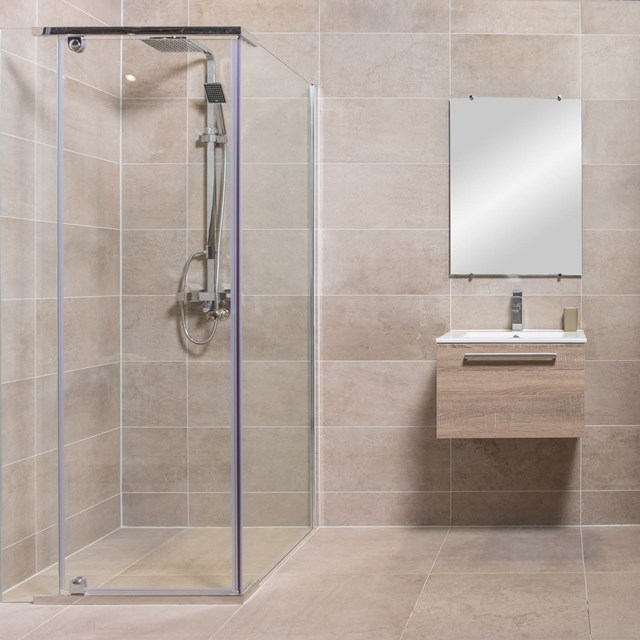 Glass corner shower cabin with chrome finish, beige tiles and floating basin; modern design for luxury bathrooms.