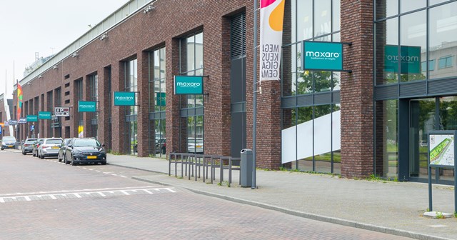 Moderne badkamer-showroom met grote glazen ramen, groene banners en een industriële bakstenen gevel.