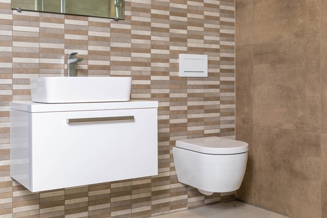 Wit hangend badkamermeubel met keramische wastafel en zwevend toilet in een modern beige betegelde badkamer.