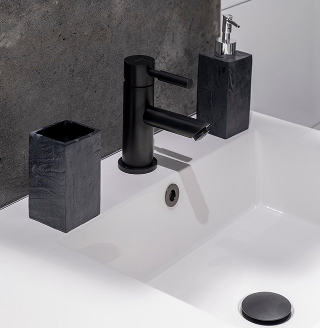 Zwarte wastafelaccessoires set van keramiek met moderne textuur, inclusief zeeppomp, beker en houder in een stijlvolle badkamer.